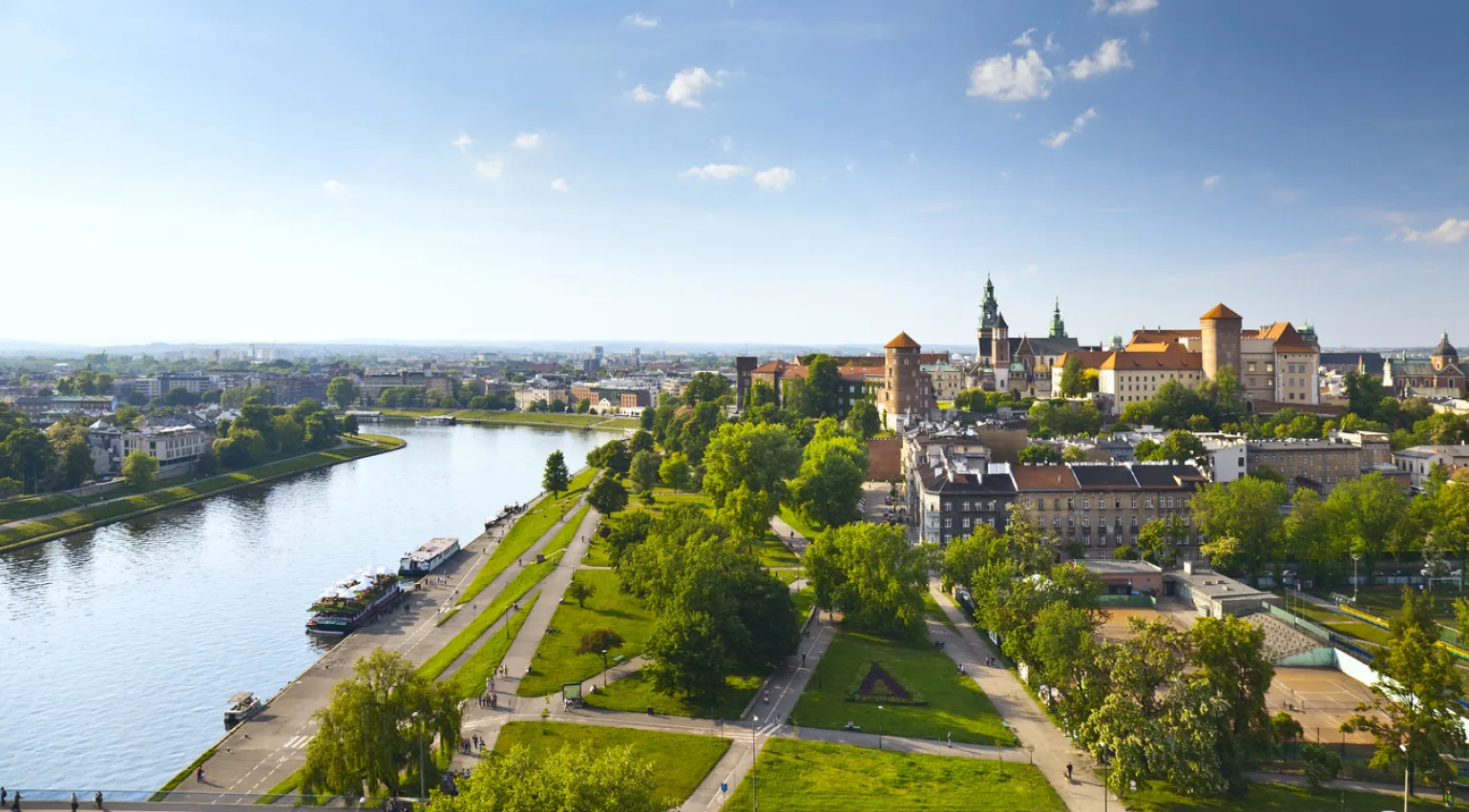 A photograph of Krakow, Poland, including a river, buildings and green space. 